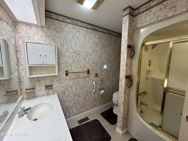 full bathroom with combined bath / shower with glass door, vanity, toilet, tile patterned floors, and a textured ceiling