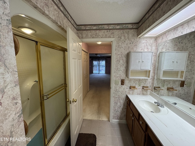 bathroom with vanity, bath / shower combo with glass door, and a textured ceiling