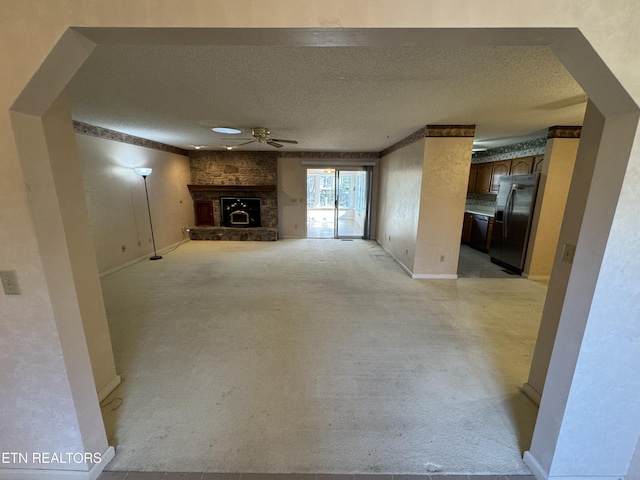 unfurnished living room with light carpet, a stone fireplace, a textured ceiling, and ceiling fan