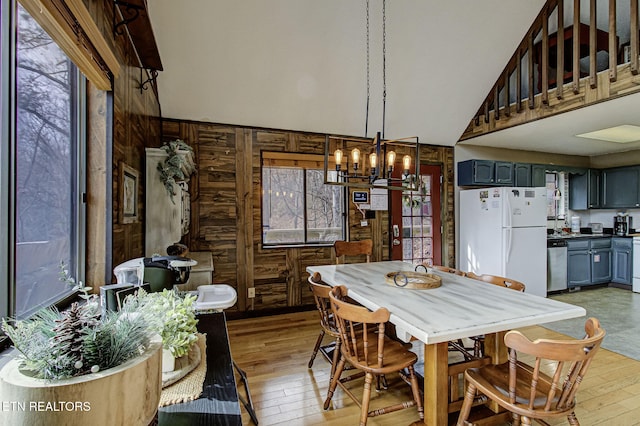 dining area featuring wood walls, high vaulted ceiling, a notable chandelier, and light wood-type flooring