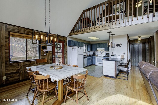 dining space with a notable chandelier, light wood-type flooring, a towering ceiling, and wooden walls