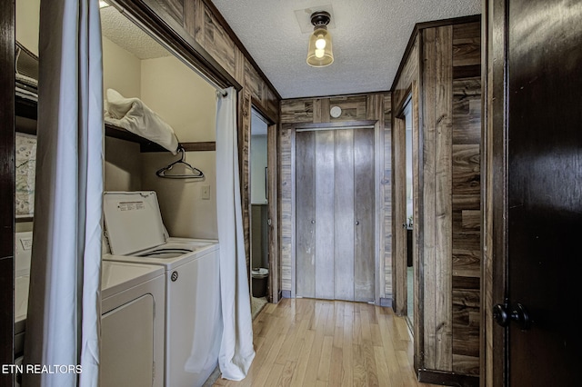 clothes washing area featuring washing machine and dryer, wooden walls, light hardwood / wood-style flooring, and a textured ceiling