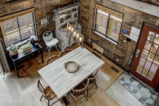 dining area featuring wood walls, hardwood / wood-style floors, and an inviting chandelier