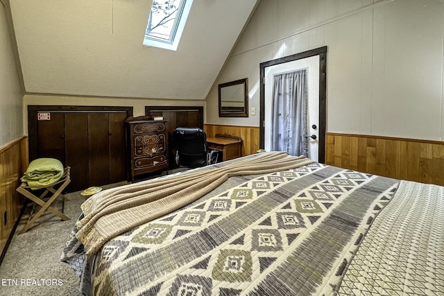 bedroom featuring carpet flooring, lofted ceiling with skylight, and wood walls