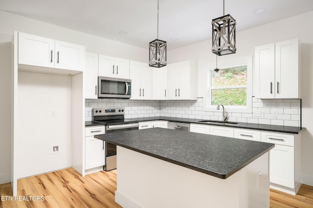 kitchen with stainless steel appliances, sink, pendant lighting, white cabinets, and a kitchen island