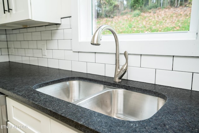 details featuring tasteful backsplash, dark stone countertops, sink, and white cabinets