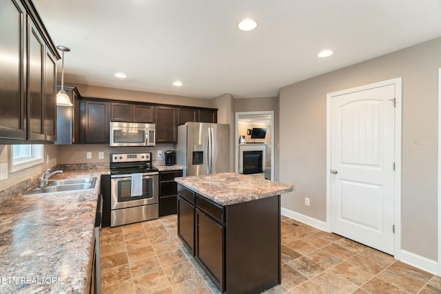 kitchen with a center island, sink, hanging light fixtures, light stone countertops, and appliances with stainless steel finishes