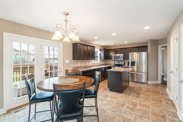 kitchen featuring dark brown cabinets, stainless steel appliances, pendant lighting, an inviting chandelier, and a kitchen island