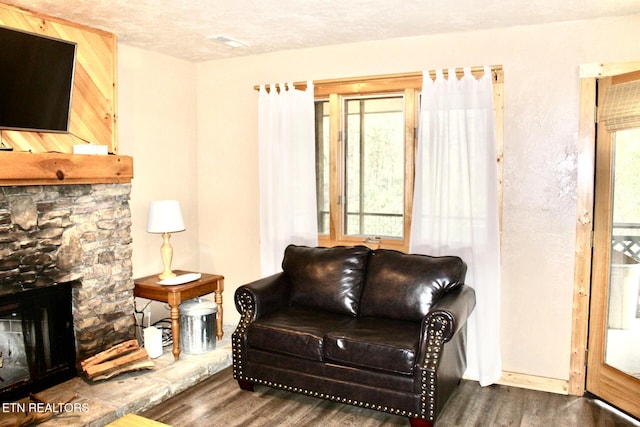 living area featuring a stone fireplace, plenty of natural light, a textured ceiling, and wood finished floors