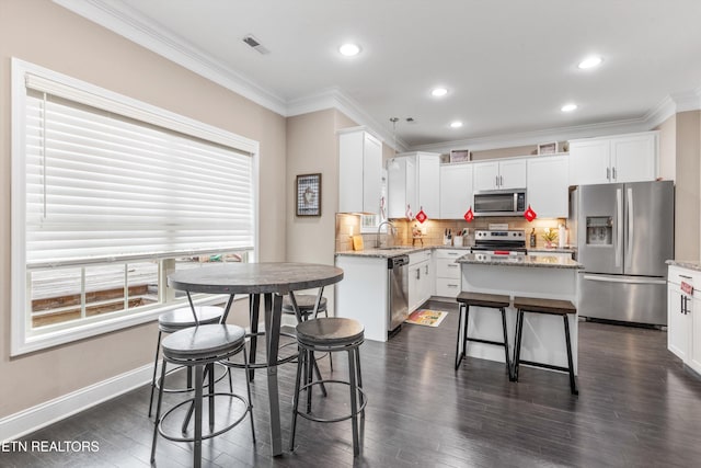 kitchen with crown molding, visible vents, appliances with stainless steel finishes, a kitchen island, and plenty of natural light