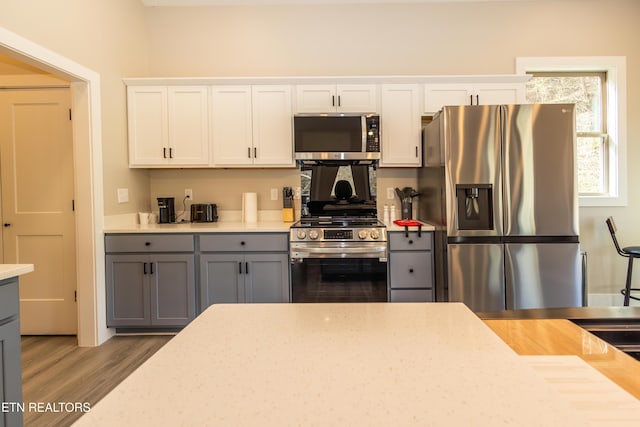 kitchen featuring gray cabinets, white cabinets, stainless steel appliances, and wood-type flooring