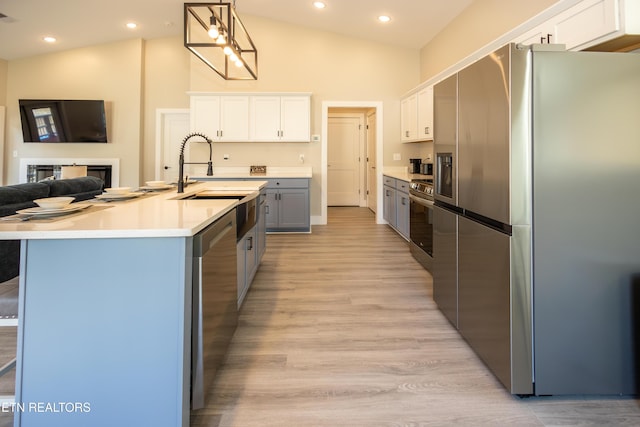 kitchen featuring high vaulted ceiling, white cabinets, an island with sink, appliances with stainless steel finishes, and decorative light fixtures