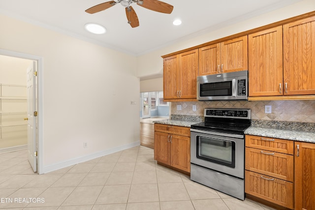 kitchen with appliances with stainless steel finishes, light tile patterned floors, light stone counters, and crown molding