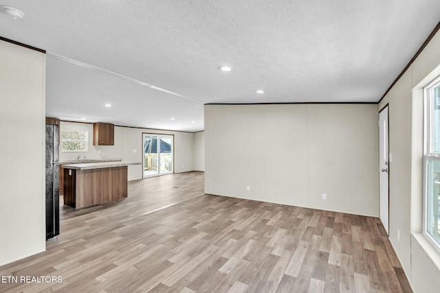 unfurnished living room featuring light wood-type flooring, crown molding, and a textured ceiling