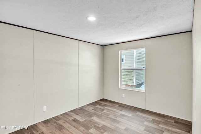 empty room featuring light wood-type flooring, ornamental molding, and a textured ceiling