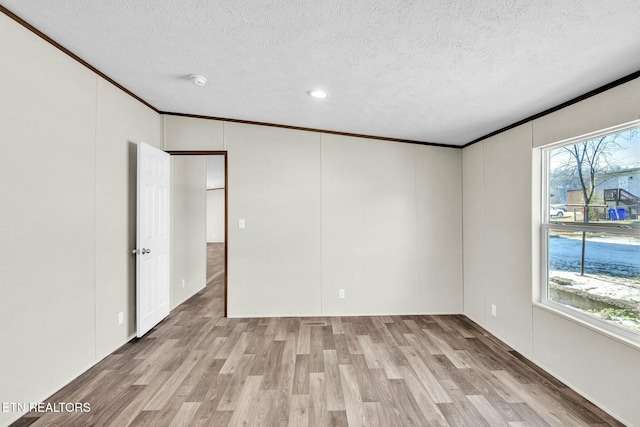 empty room with a healthy amount of sunlight, ornamental molding, a textured ceiling, and light hardwood / wood-style flooring