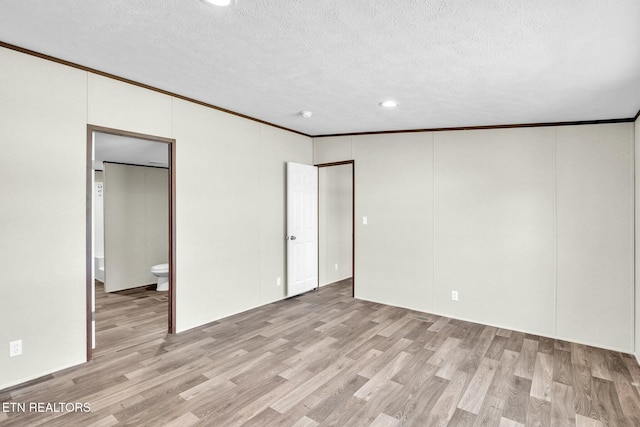 unfurnished bedroom with a textured ceiling, ornamental molding, ensuite bath, and light wood-type flooring