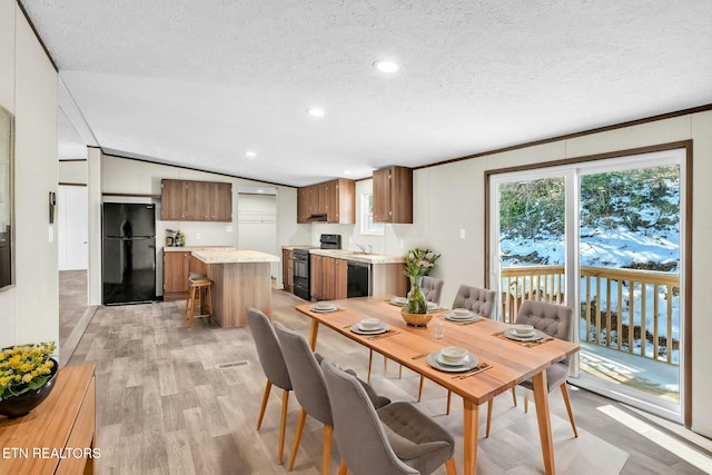 dining area featuring lofted ceiling, a textured ceiling, crown molding, light hardwood / wood-style flooring, and sink