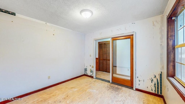 spare room with a textured ceiling, light wood-type flooring, and a healthy amount of sunlight