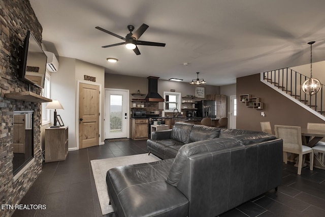 living room featuring ceiling fan with notable chandelier, a stone fireplace, an AC wall unit, and sink