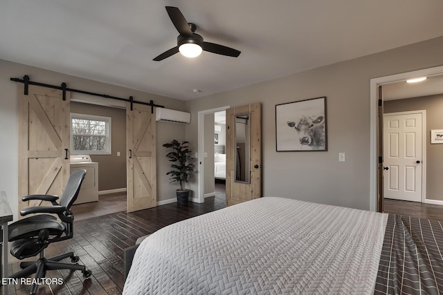 bedroom with an AC wall unit, ensuite bath, ceiling fan, a barn door, and washer / dryer