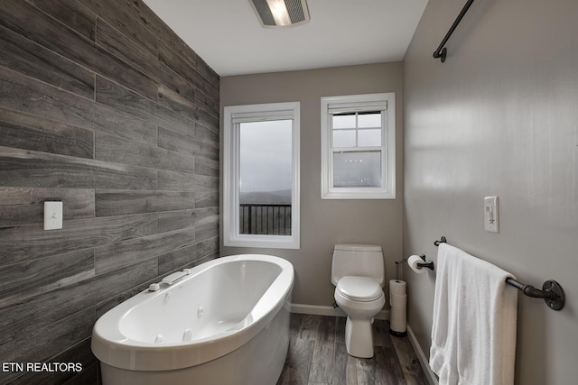 bathroom featuring toilet, wood-type flooring, a bath, and wooden walls