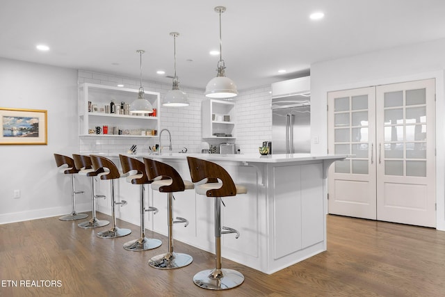 kitchen featuring a breakfast bar, wood-type flooring, built in refrigerator, white cabinetry, and hanging light fixtures