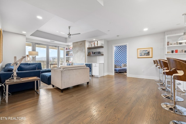 living room with dark hardwood / wood-style floors, ceiling fan, wine cooler, and a tray ceiling