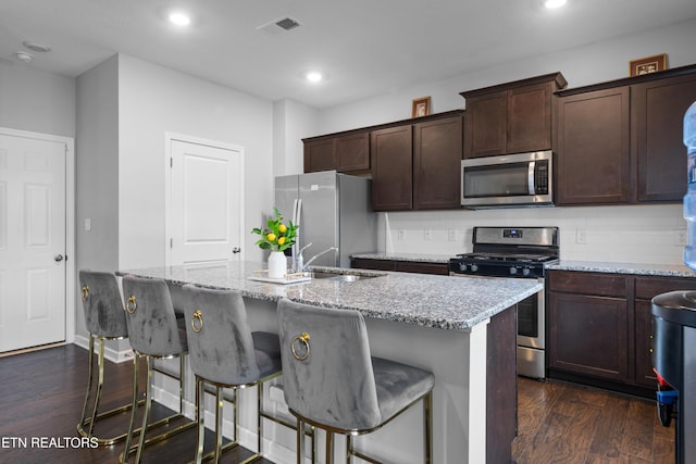 kitchen featuring dark wood-type flooring, stainless steel appliances, light stone countertops, and a center island with sink