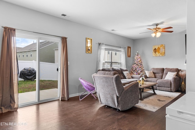 living room with a wealth of natural light, dark wood-type flooring, and ceiling fan