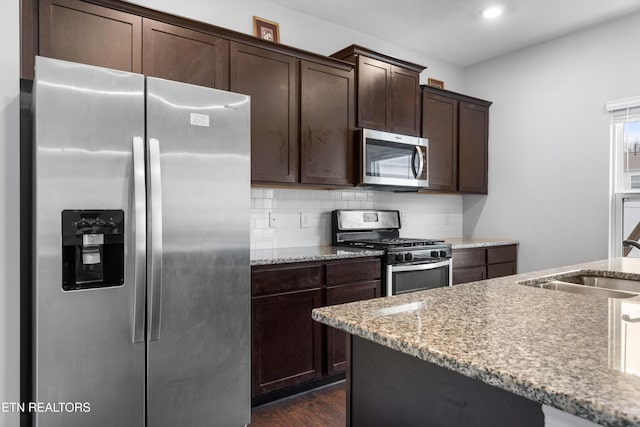 kitchen featuring sink, dark hardwood / wood-style flooring, light stone counters, dark brown cabinets, and stainless steel appliances