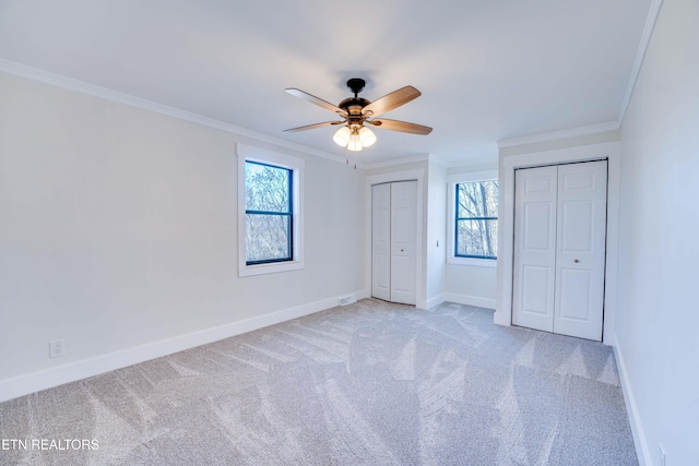 unfurnished bedroom with multiple closets, crown molding, ceiling fan, and light colored carpet