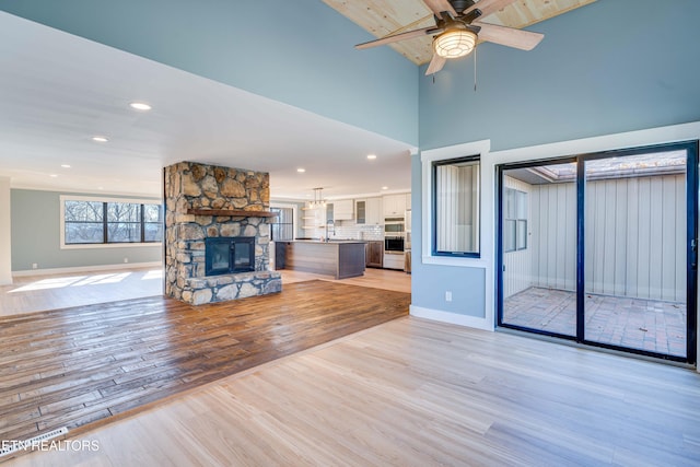 unfurnished living room featuring light wood-type flooring, a stone fireplace, ceiling fan, and sink