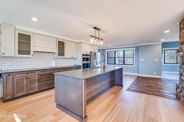 kitchen featuring sink, light hardwood / wood-style floors, decorative light fixtures, a center island with sink, and appliances with stainless steel finishes