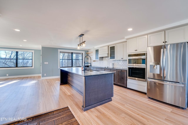 kitchen featuring a center island with sink, sink, light hardwood / wood-style flooring, appliances with stainless steel finishes, and decorative light fixtures