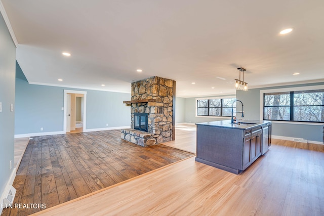 kitchen with decorative light fixtures, a fireplace, sink, and light hardwood / wood-style flooring