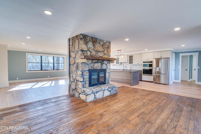 unfurnished living room featuring a fireplace, light wood-type flooring, ornamental molding, and sink