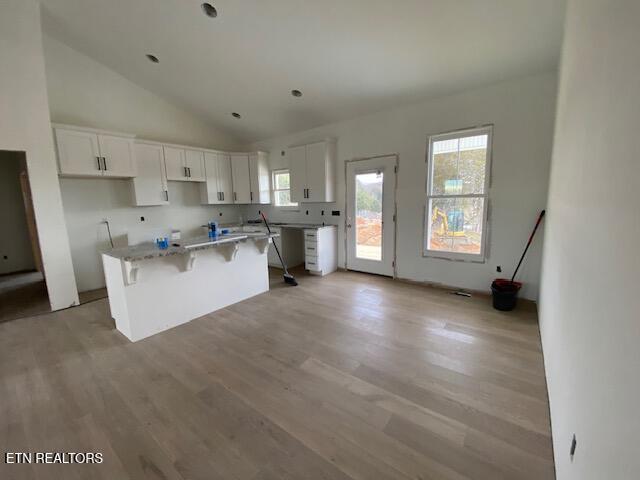 kitchen featuring a kitchen island, white cabinetry, light hardwood / wood-style floors, light stone counters, and a breakfast bar