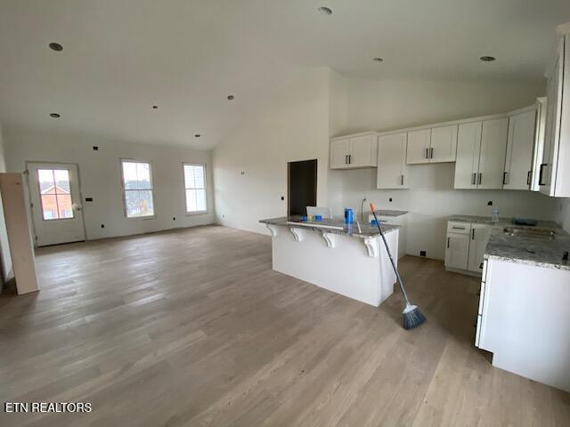 kitchen with a kitchen island, light wood-type flooring, light stone countertops, high vaulted ceiling, and white cabinets