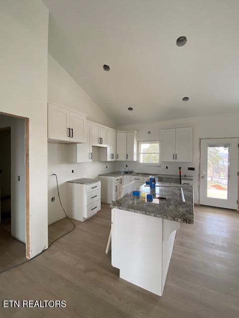 kitchen featuring light wood-type flooring, dark stone counters, high vaulted ceiling, a kitchen island, and white cabinets