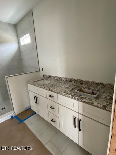 bathroom featuring tile patterned flooring, a tile shower, and vanity