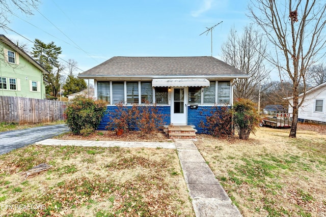 bungalow-style home featuring a shingled roof, a front lawn, and fence