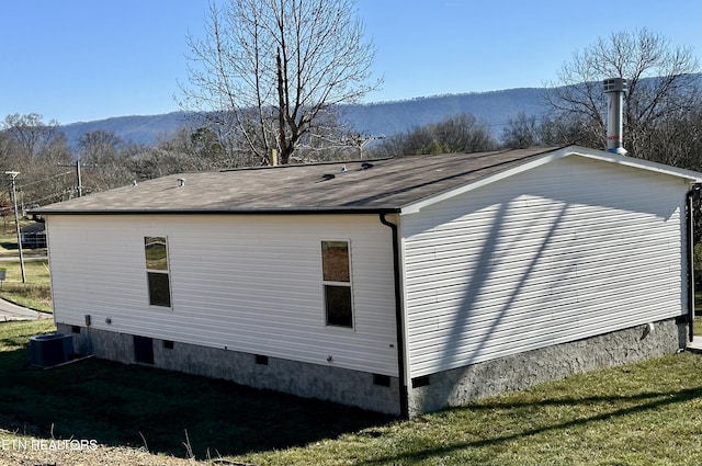 view of side of home with a lawn, a mountain view, and central AC