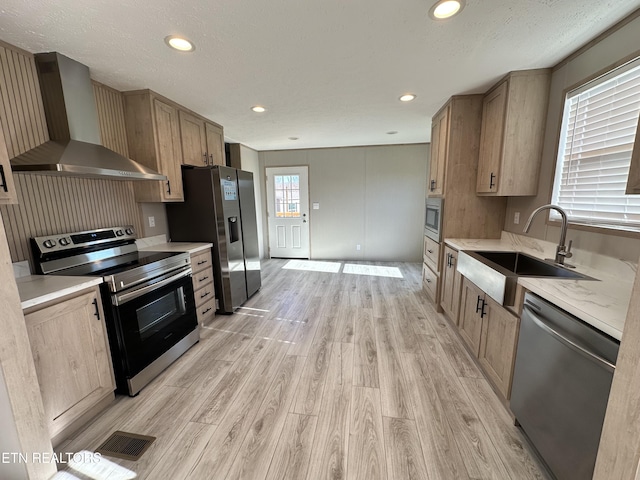 kitchen with sink, wall chimney exhaust hood, a textured ceiling, appliances with stainless steel finishes, and light hardwood / wood-style floors