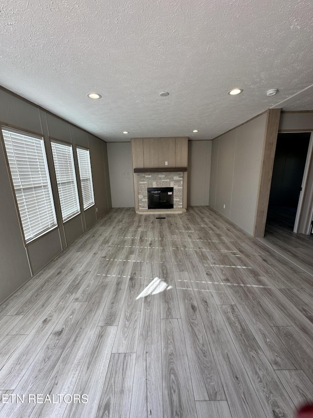 unfurnished living room featuring a stone fireplace, light hardwood / wood-style floors, and a textured ceiling