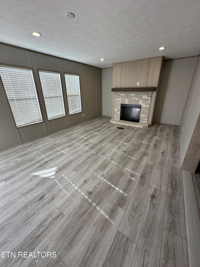 unfurnished living room featuring a stone fireplace, light hardwood / wood-style flooring, and a textured ceiling