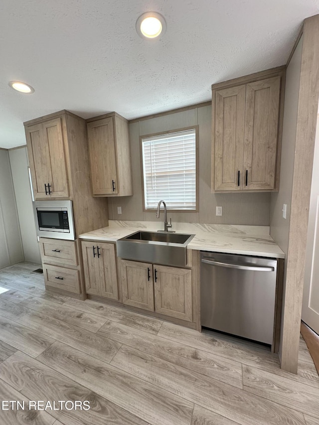 kitchen with sink, light hardwood / wood-style floors, a textured ceiling, light brown cabinetry, and appliances with stainless steel finishes