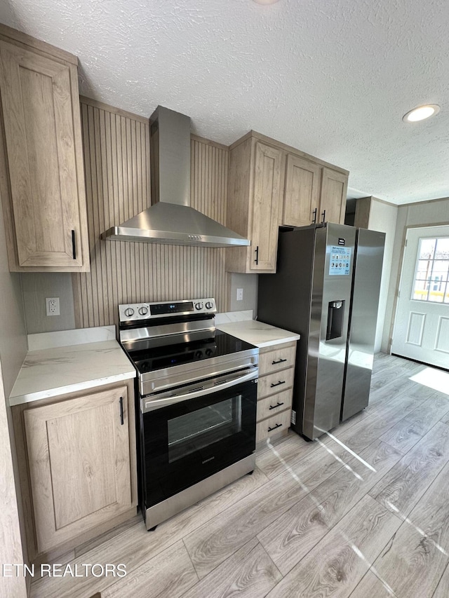 kitchen featuring appliances with stainless steel finishes, light wood-type flooring, wall chimney exhaust hood, a textured ceiling, and light brown cabinets