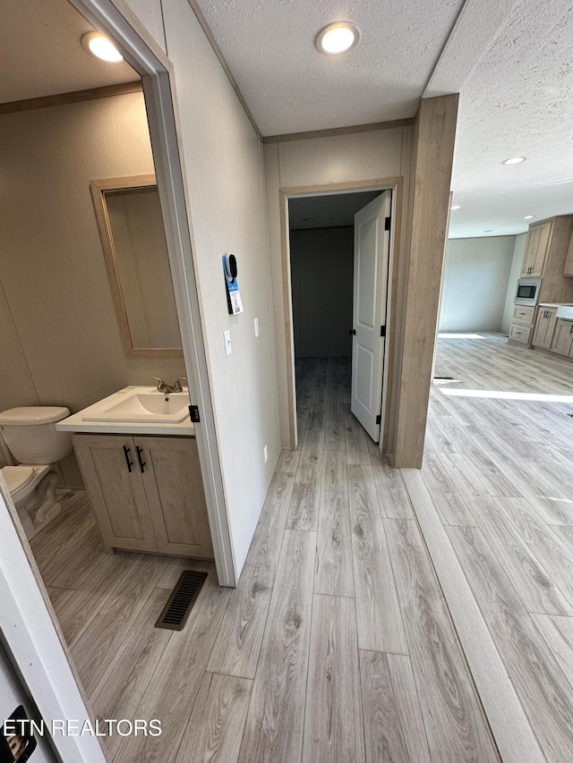 corridor with a textured ceiling, crown molding, light wood-type flooring, and sink