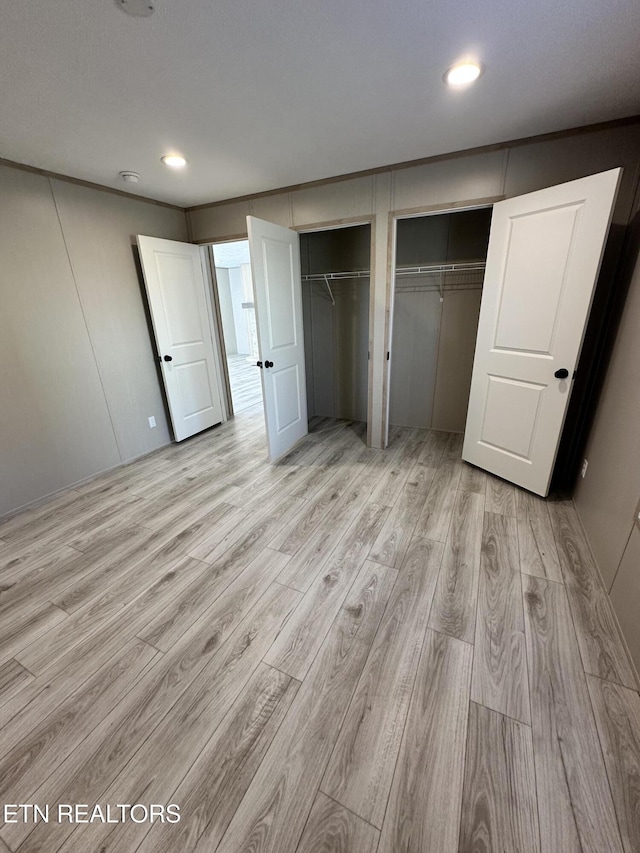 unfurnished bedroom featuring two closets and light wood-type flooring